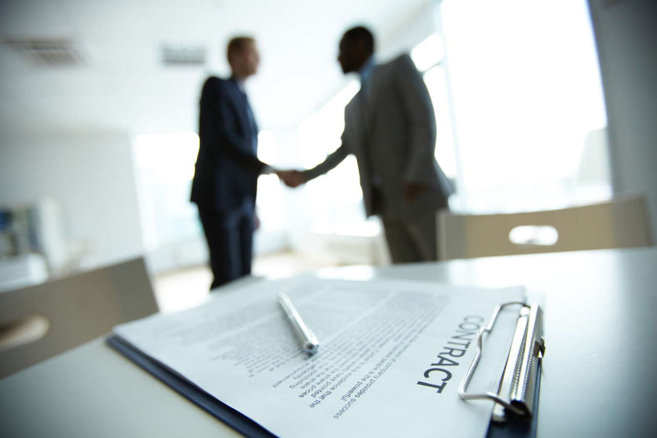 Image of business contract on background of two employees handsh